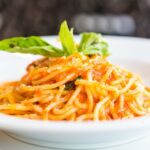 A delicious bowl of spaghetti topped with fresh basil, cherry tomatoes, and Parmesan cheese on a rustic wooden table