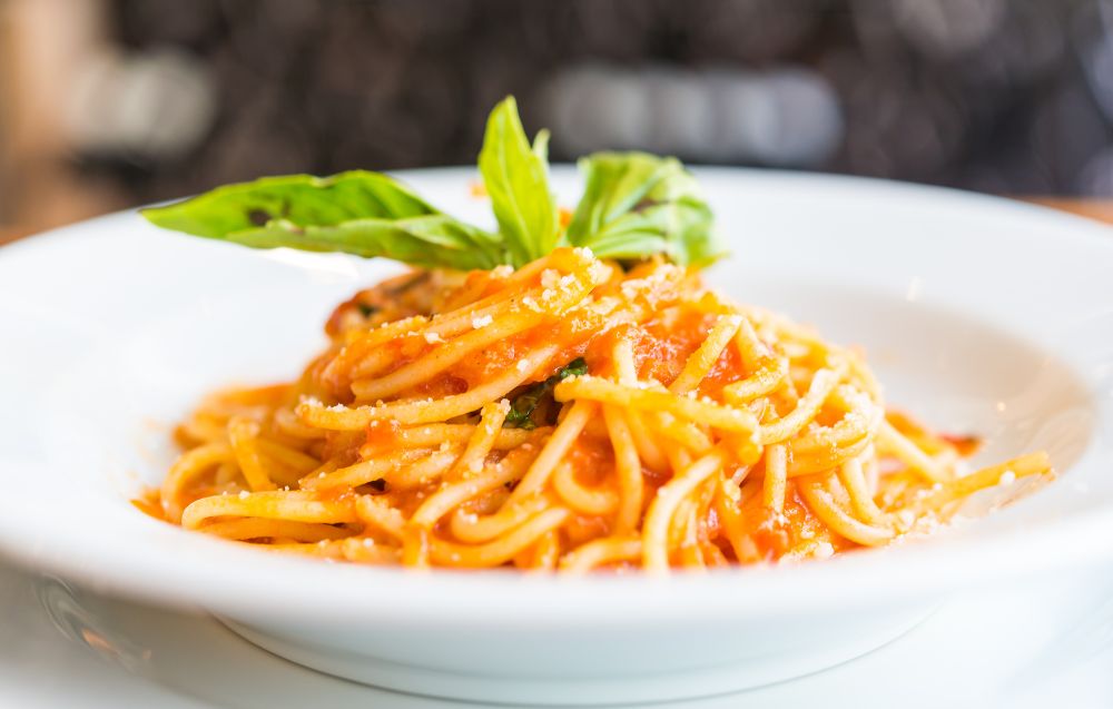 A delicious bowl of spaghetti topped with fresh basil, cherry tomatoes, and Parmesan cheese on a rustic wooden table